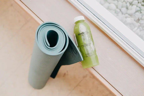 Rolled blue yoga mat beside a GLJ Glo bottle on a wooden surface.